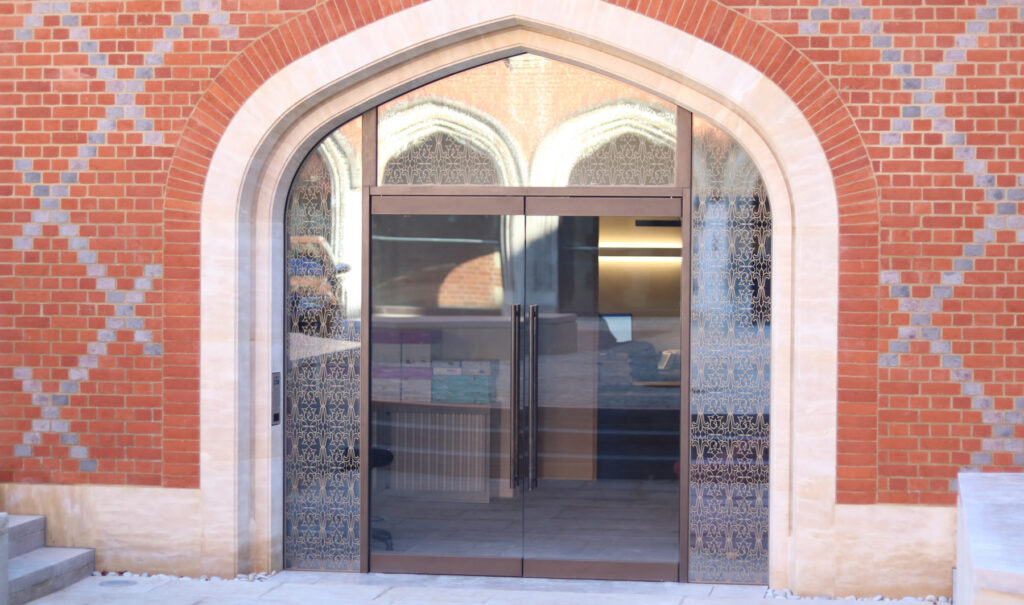 Glass double doors with decorative metal grille, set in an arched brick facade above a stone threshold